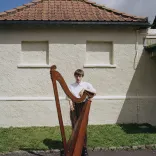 Harpist Cerys Hafana standing with her harp in front of Pontypridd Lido