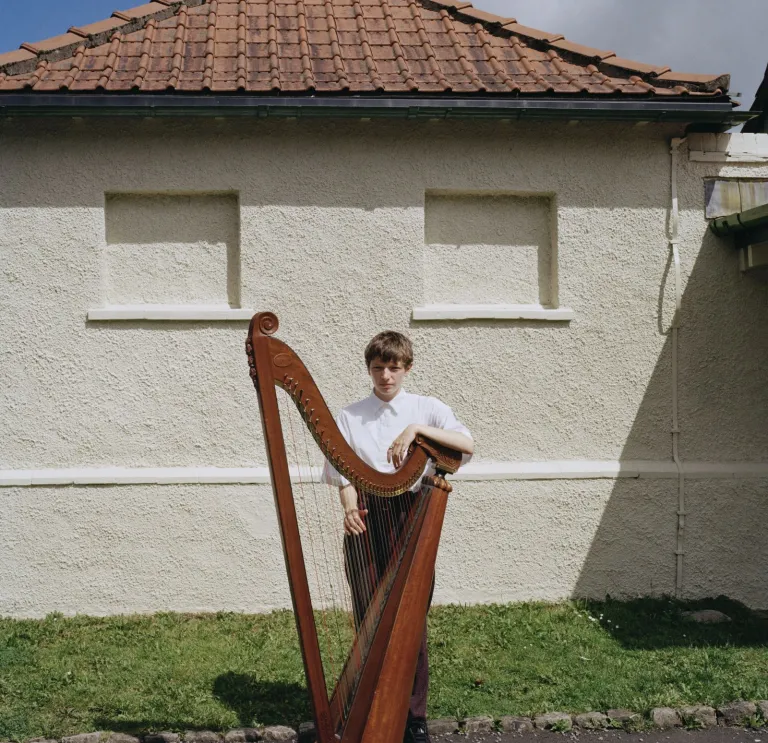 Harpist Cerys Hafana standing with her harp in front of Pontypridd Lido