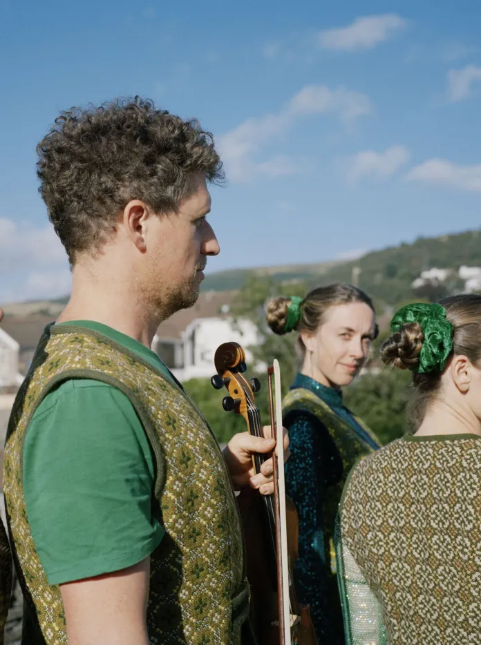 Four performers dressed in traditional Welsh garments standing outside against a blue sky
