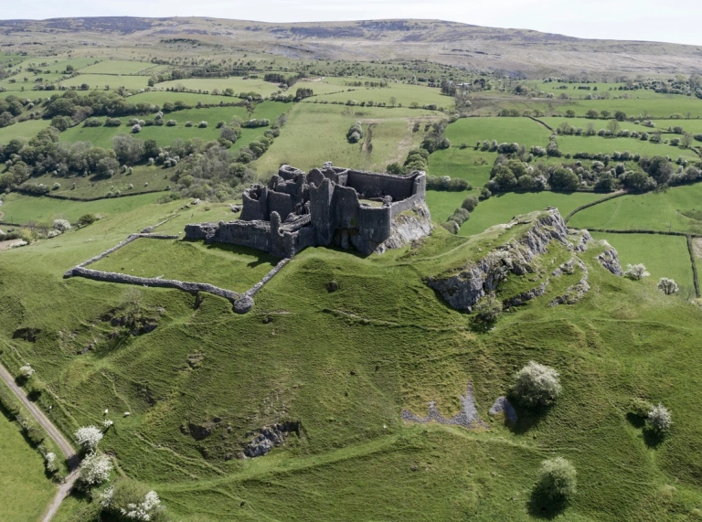 Ruines d'un château entourées de champs verts et de montagnes.