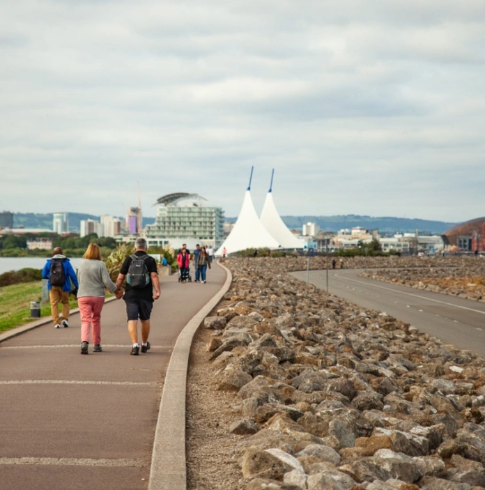 A scenic shot of people walking along a pathway with water and large buildings in the distance