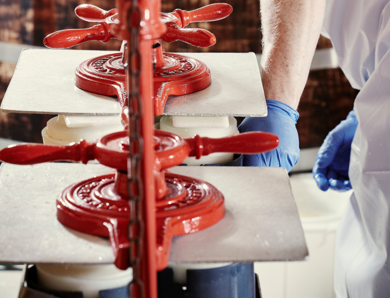 An employee working with a cheese press in a warehouse