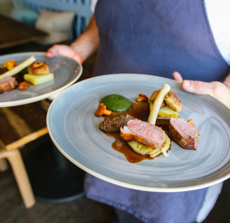 Ein Koch, der zwei Teller mit Essen trägt.